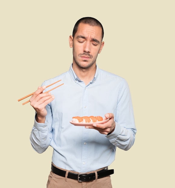 Jeune homme à l'aide de baguettes pour manger des sushis