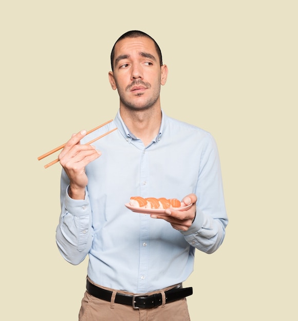 Jeune homme à l'aide de baguettes pour manger des sushis