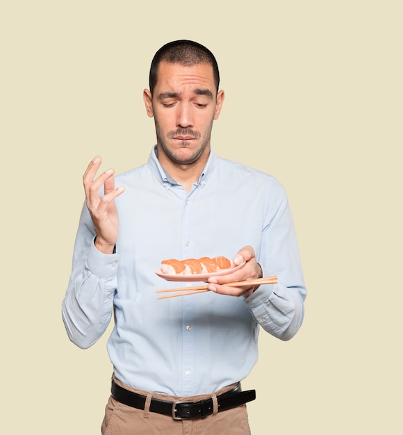 Jeune homme à l'aide de baguettes pour manger des sushis