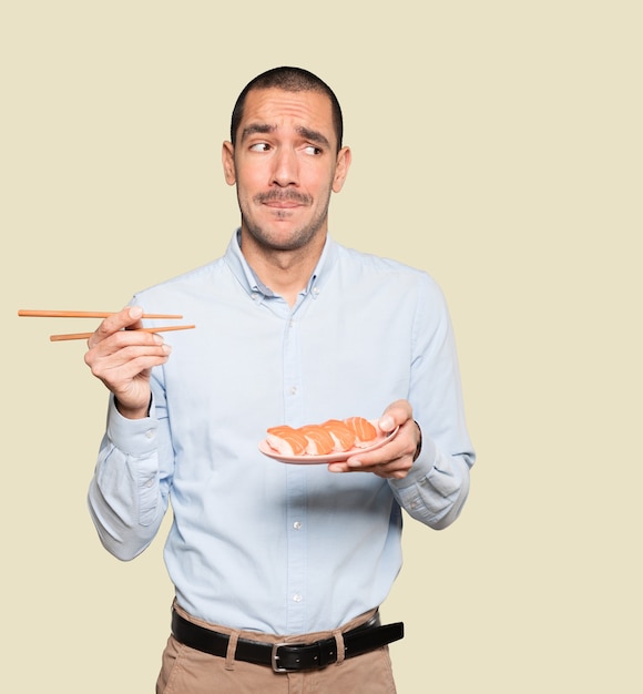 Jeune homme à l'aide de baguettes pour manger des sushis