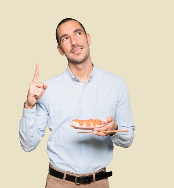 Jeune homme à l'aide de baguettes pour manger des sushis