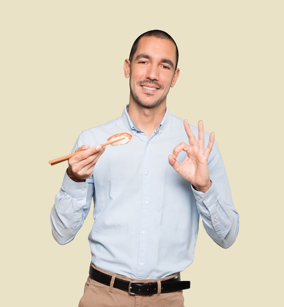 Jeune homme à l'aide de baguettes pour manger des sushis