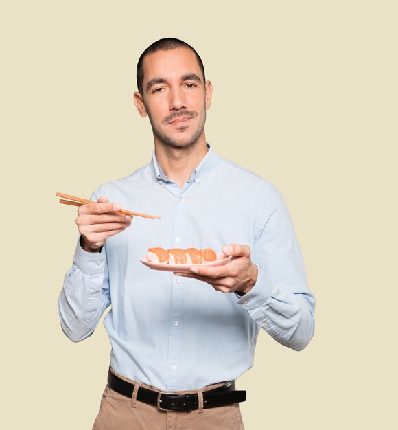 Jeune homme à l'aide de baguettes pour manger des sushis