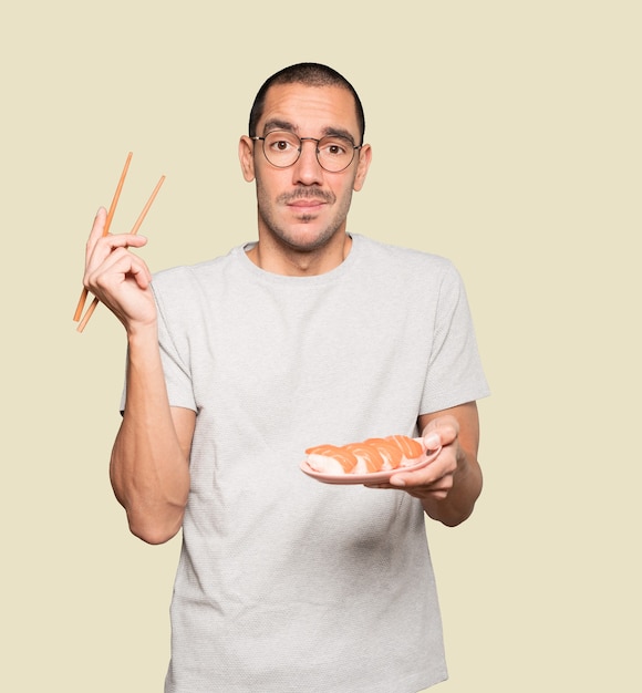 Jeune homme à l'aide de baguettes pour manger des sushis