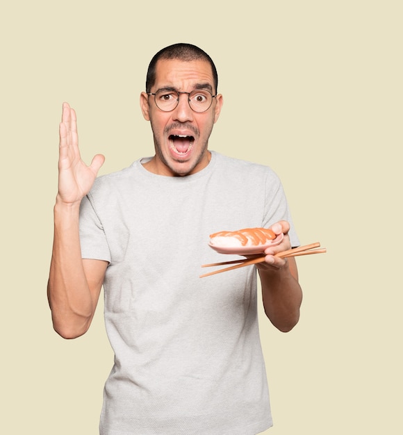 Jeune homme à l'aide de baguettes pour manger des sushis