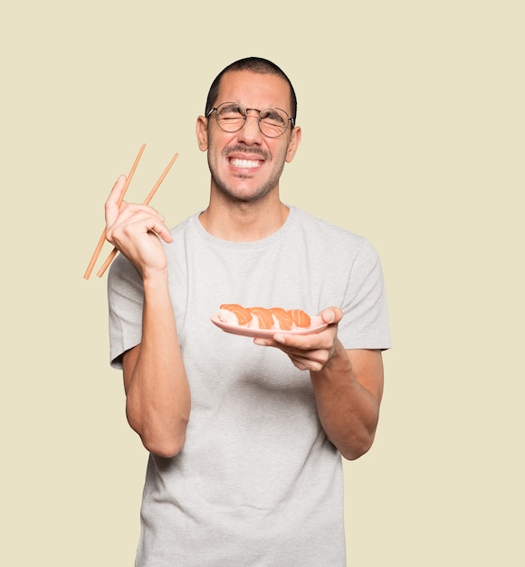 Jeune homme à l'aide de baguettes pour manger des sushis