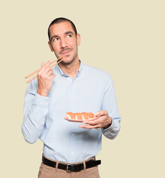 Jeune homme à l'aide de baguettes pour manger des sushis