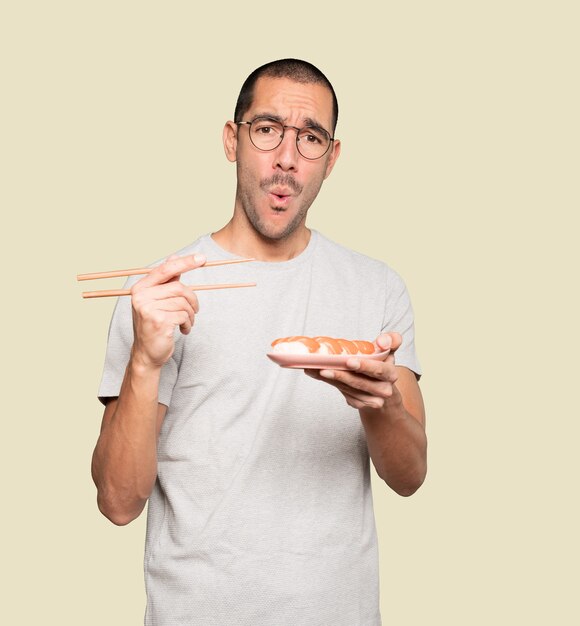 Jeune homme à l'aide de baguettes pour manger des sushis