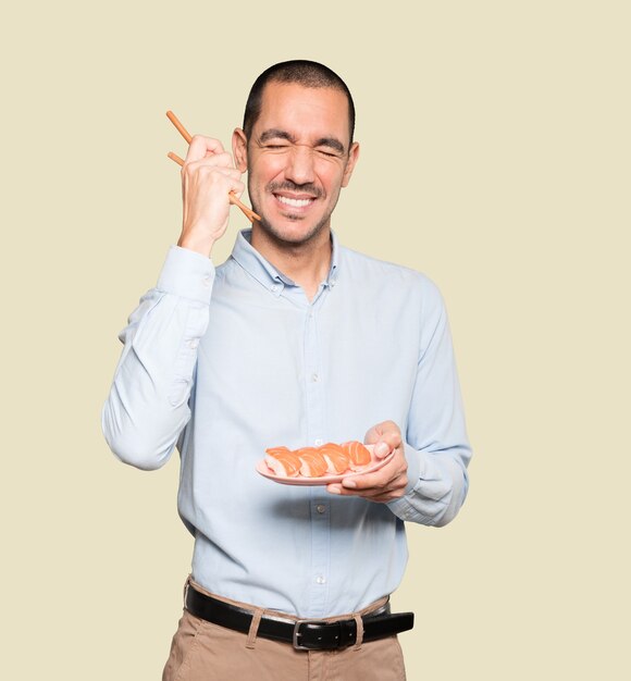 Jeune homme à l'aide de baguettes pour manger des sushis