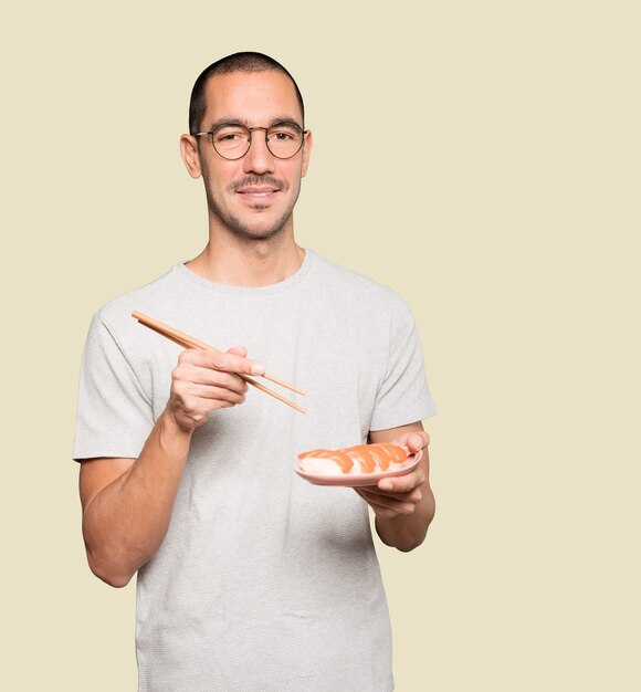 Jeune homme à l'aide de baguettes pour manger des sushis