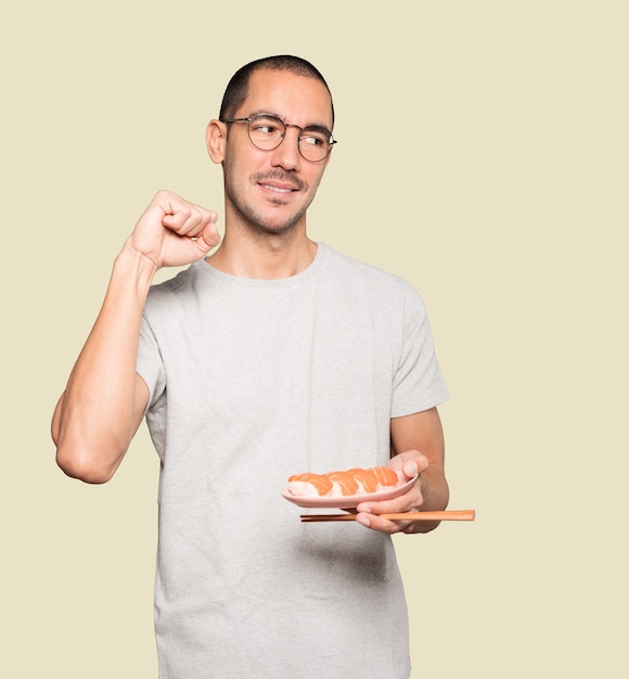 Jeune homme à l'aide de baguettes pour manger des sushis