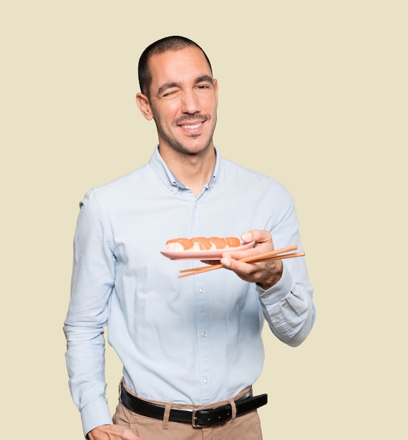 Jeune homme à l'aide de baguettes pour manger des sushis