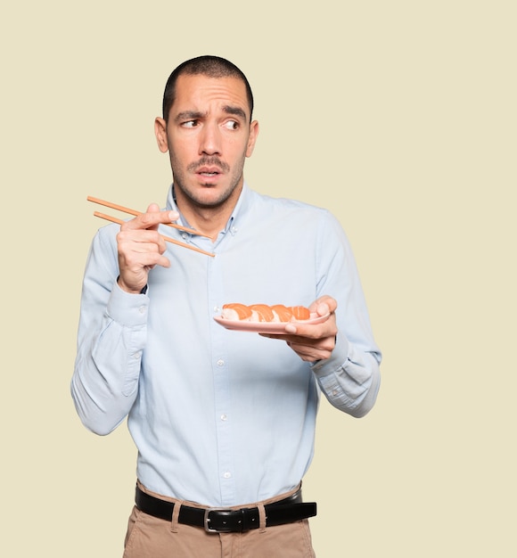 Jeune homme à l'aide de baguettes pour manger des sushis