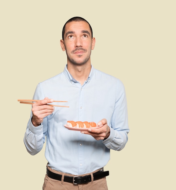 Jeune homme à l'aide de baguettes pour manger des sushis