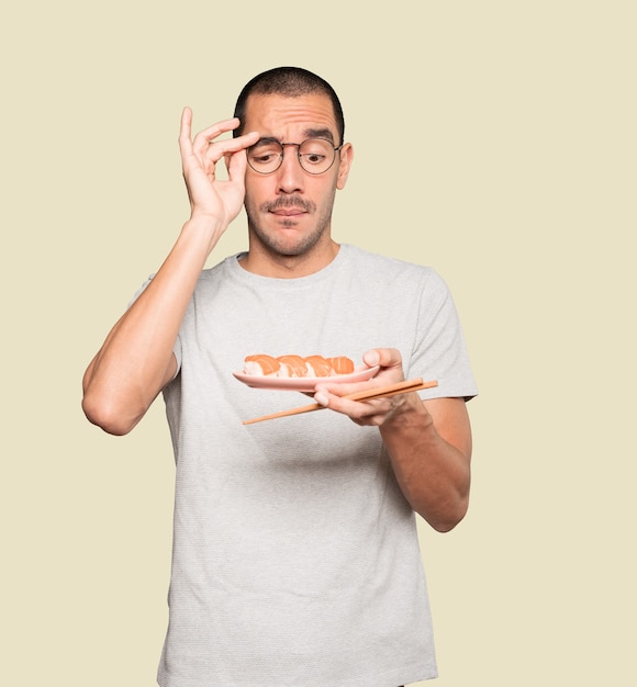 Jeune homme à l'aide de baguettes pour manger des sushis