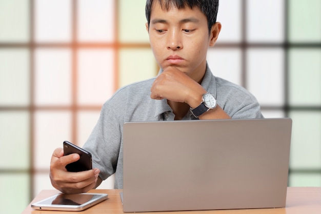 Jeune homme à l'aide d'un smartphone et d'un ordinateur portable dans le bâtiment intérieur.