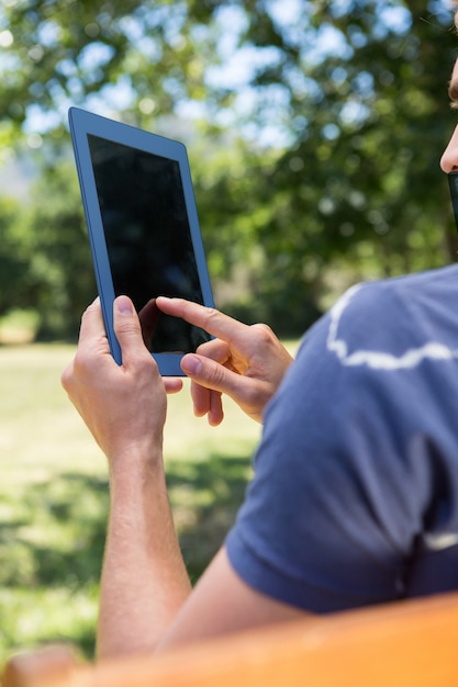 Jeune homme à l&#39;aide de tablette sur le banc de parc