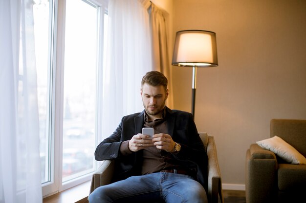 Jeune homme à l&#39;aide de téléphone portable dans la chambre par la fenêtre