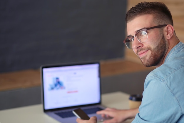 Jeune homme à l'aide de téléphone et travaille sur l'ordinateur portable.