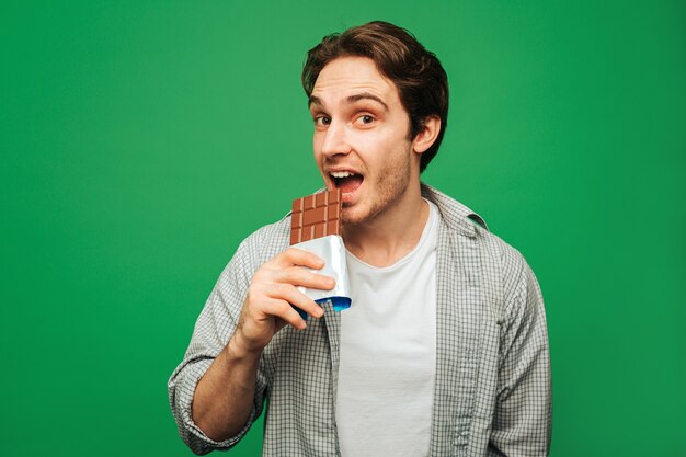 Jeune homme aime manger une barre de chocolat