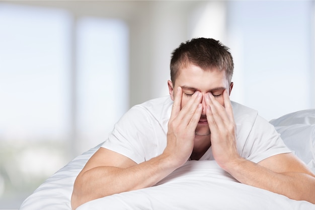 Jeune homme allongé dans son lit avec les mains sur le visage dans la chambre