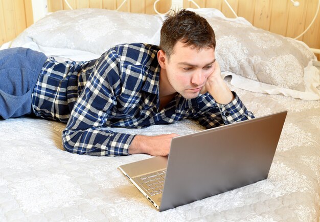 Jeune homme allongé sur un lit et regardant un ordinateur portable à la maison