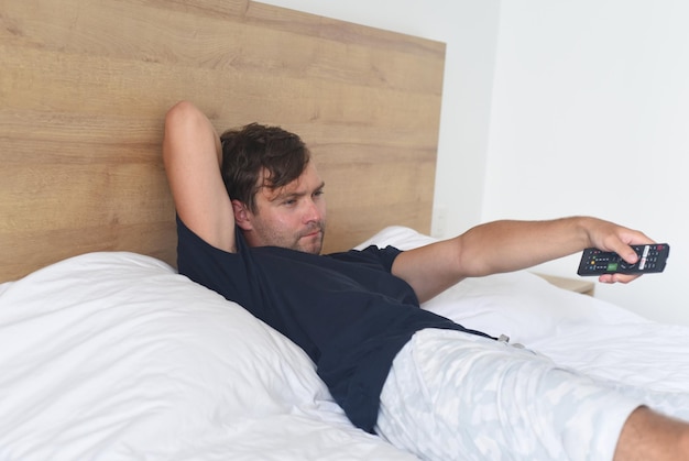 Jeune homme allongé sur un lit et tenant la télécommande du téléviseur