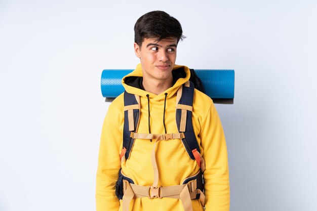 Jeune homme alpiniste avec un gros sac à dos sur un mur bleu et debout sur le côté