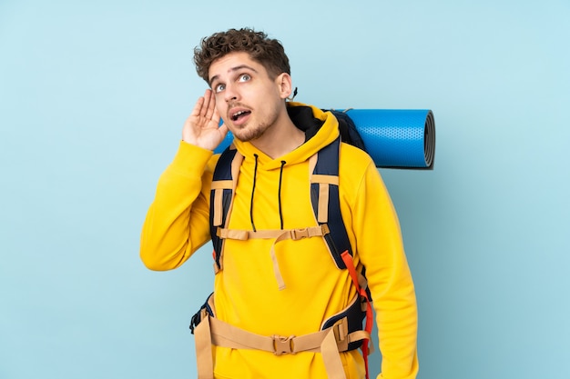 Jeune homme alpiniste avec un gros sac à dos sur le mur bleu en écoutant quelque chose