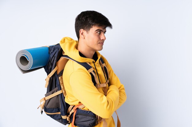 Jeune homme alpiniste avec un gros sac à dos sur le mur bleu en riant