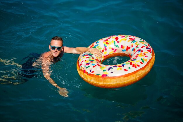 Jeune homme sur un anneau gonflable dans la mer se reposant et nageant par une journée ensoleillée