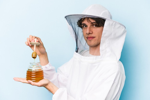 Jeune homme apiculteur caucasien tenant du miel isolé sur fond bleu
