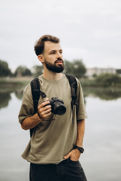 Un jeune homme avec un appareil photo reflex moderne dans les mains sur un fond naturel