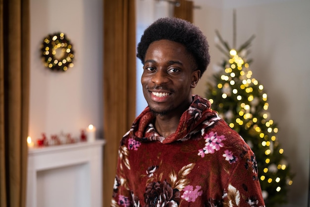 Un jeune homme d'apparence africaine sourit sincèrement un arbre de noël scintille dans la pièce