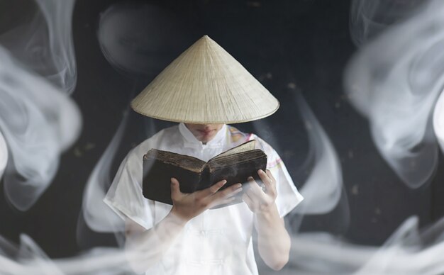 Le jeune homme d'apparence asiatique dans un kimono prie avec un livre