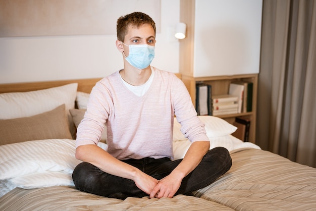 Un jeune homme d'apparence européenne assis confortablement sur le canapé dans un concept de masque médical pour attendre...