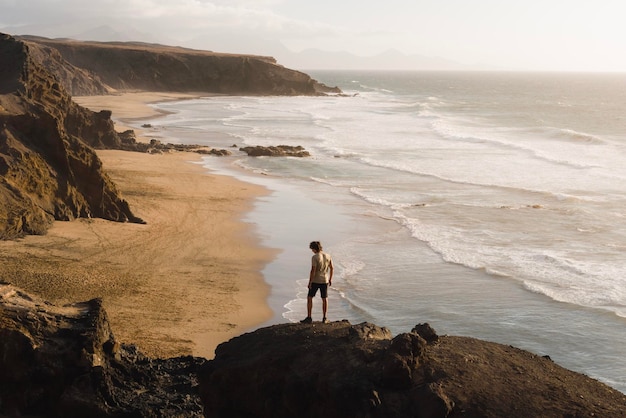 Photo le jeune homme apprécie le coucher du soleil sur la côte de fuerteventura tout en visitant les îles canaries