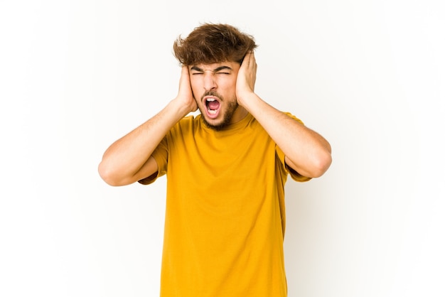 Jeune homme arabe sur blanc couvrant les oreilles avec les mains en essayant de ne pas entendre un son trop fort.