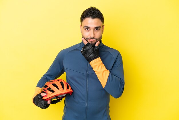 Jeune homme arabe cycliste isolé sur fond jaune pensant