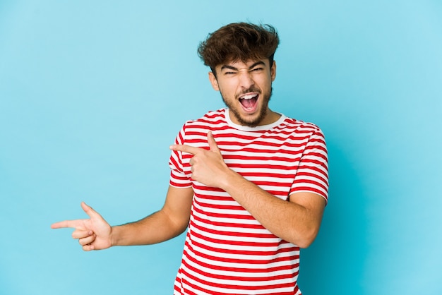 Jeune homme arabe sur fond bleu pointant avec l'index vers un espace de copie, exprimant l'excitation et le désir.