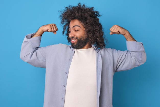 Un jeune homme arabe fort prend la pose d'un homme fort et montre les biceps en studio