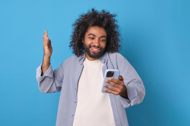 Jeune homme arabe heureux avec un téléphone fait de la vague avec la main se tient dans le studio