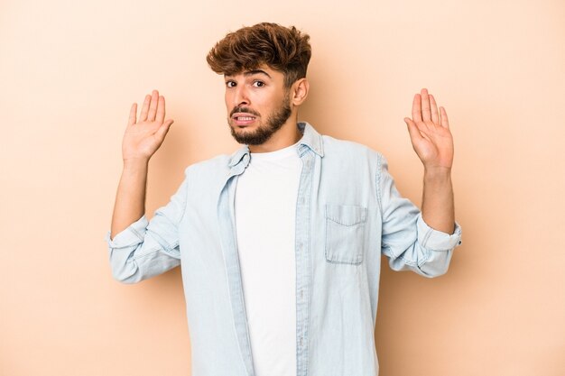 Jeune homme arabe isolé sur fond beige choqué en raison d'un danger imminent