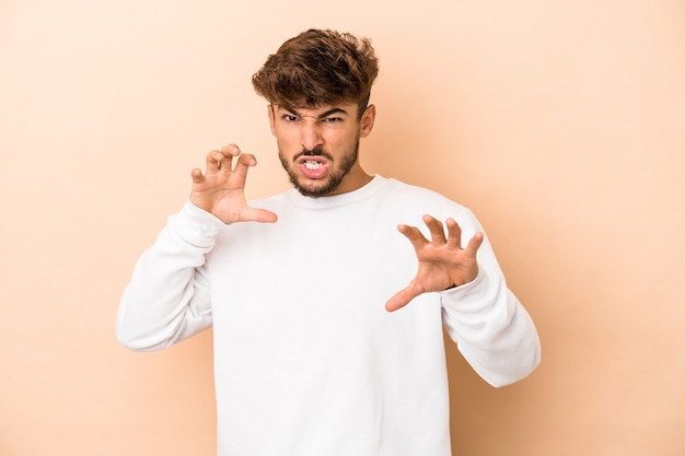 Jeune homme arabe isolé sur fond beige montrant des griffes imitant un chat, geste agressif.