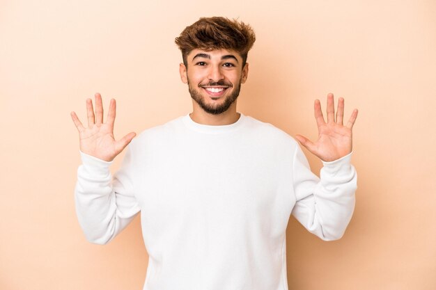 Jeune homme arabe isolé sur fond beige montrant le numéro dix avec les mains.