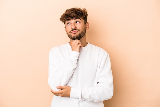 Jeune homme arabe isolé sur fond beige pensant et levant, réfléchissant, contemplant, ayant un fantasme.