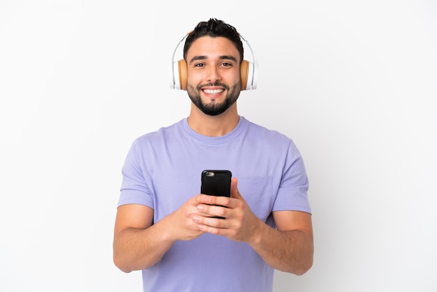 Jeune homme arabe isolé sur fond blanc, écouter de la musique avec un mobile et à l'avant