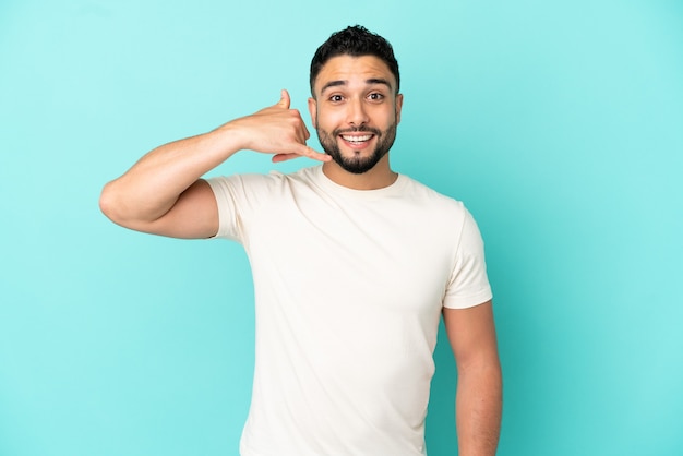 Jeune homme arabe isolé sur fond bleu faisant un geste de téléphone. Rappelle-moi signe