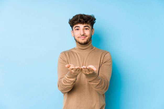 Jeune homme arabe isolé tenant quelque chose avec des palmiers, offrant