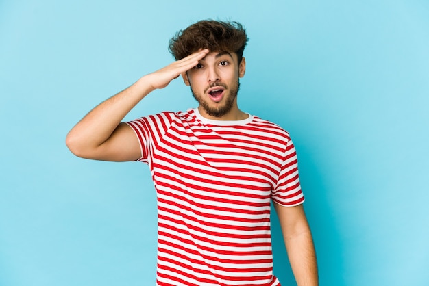 Jeune homme arabe sur le mur bleu crie fort, garde les yeux ouverts et les mains tendues.